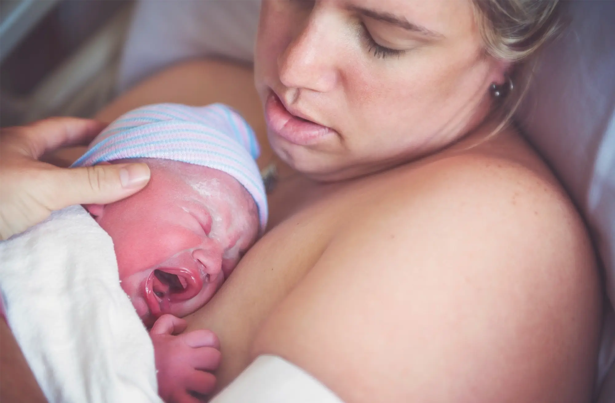 Newborn baby crying while resting skin-to-skin on their parent’s chest.